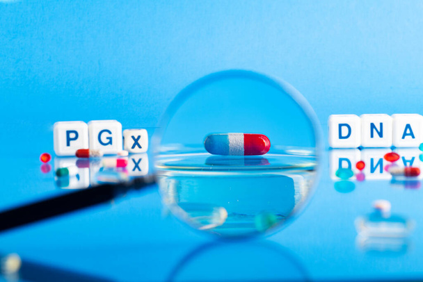 DNA pill on the background of a laboratory table with medicines and preparations. View through a magnifying glass. On a blue background. Selective focus. - Fotoğraf, Görsel