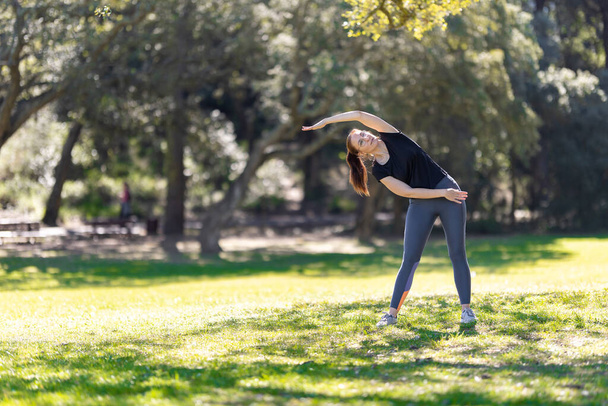 An adult woman in sports doing fitness exercise in the park. Mid shot - Photo, Image