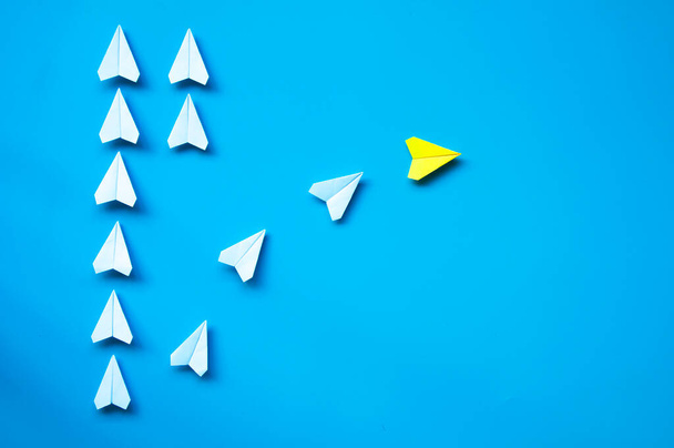 Желтая бумага самолета оригами оставив с другими белыми самолетами на синем фоне с настраиваемым пространством для текста или идей. Концепция лидерских навыков и пространство для копирования. - Фото, изображение