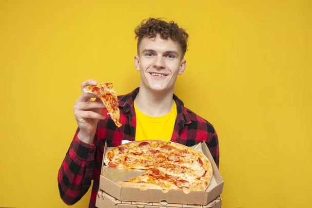 student eats pizza on a yellow background, a young curly guy advertises fast food and smiles - Photo, Image