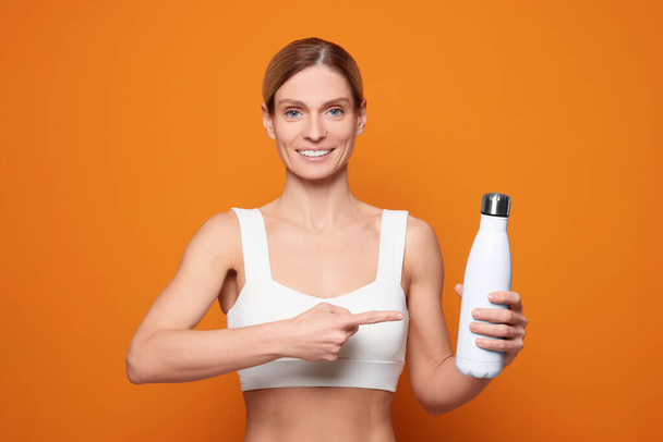 Sportswoman with thermo bottle on orange background - Fotoğraf, Görsel