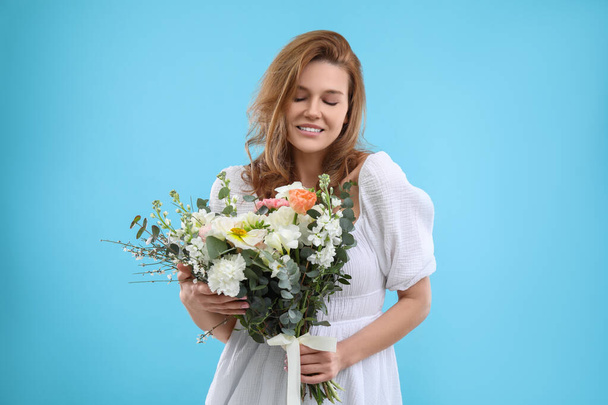 Beautiful woman with bouquet of flowers on light blue background - Photo, Image