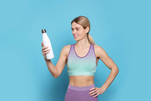 Sportswoman with thermo bottle on light blue background - Valokuva, kuva