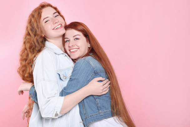 Portrait of beautiful young redhead sisters on pink background. Space for text - 写真・画像