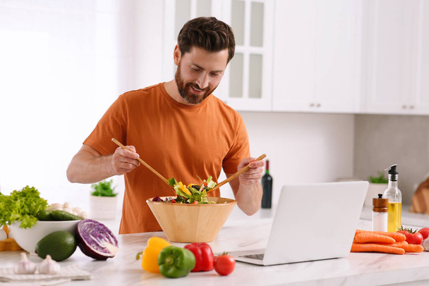 Man making dinner while watching online cooking course via laptop in kitchen - Foto, Imagem
