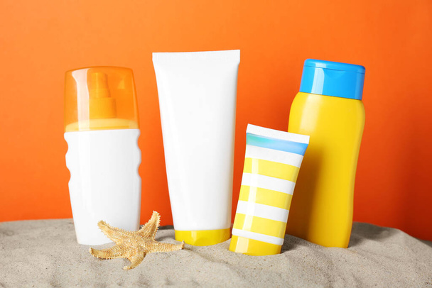 Different suntan products and starfish on sand against orange background - Φωτογραφία, εικόνα