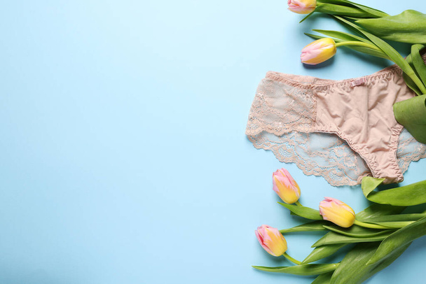Elegant beige women's underwear and beautiful tulips on light blue background, flat lay. Space for text - Foto, imagen