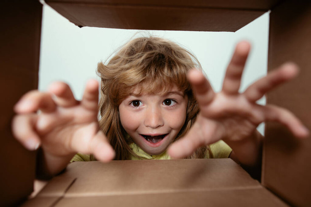 Funny excited child unpacking and opening the carton box looking inside. The little kids unboxing gift inside view. Child boy looking surprised into a gift - Foto, Imagem
