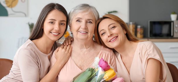 Mature woman with her mother and daughter with flowers at home - Фото, зображення