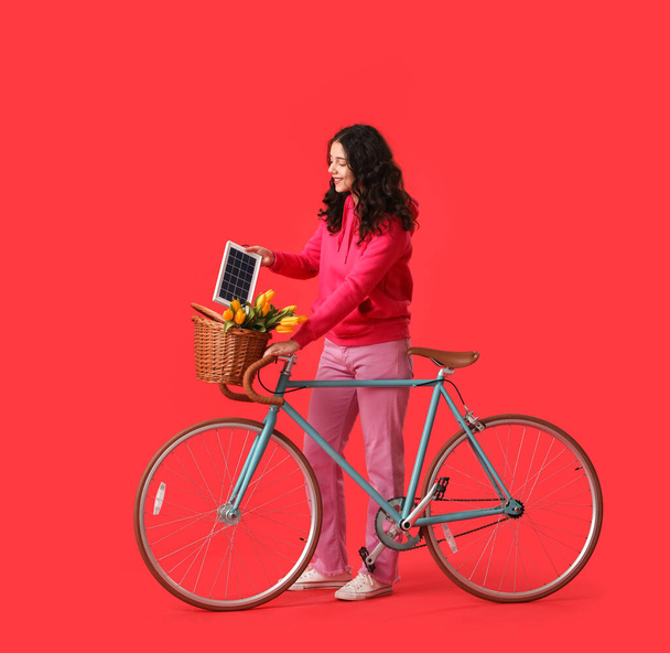 Девочка-подросток с велосипедом и портативной солнечной панелью на красном фоне - Фото, изображение