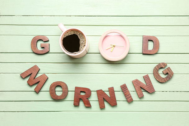 Text GOOD MORNING made of letters, cup with coffee and alarm clock on color wooden background - Fotoğraf, Görsel