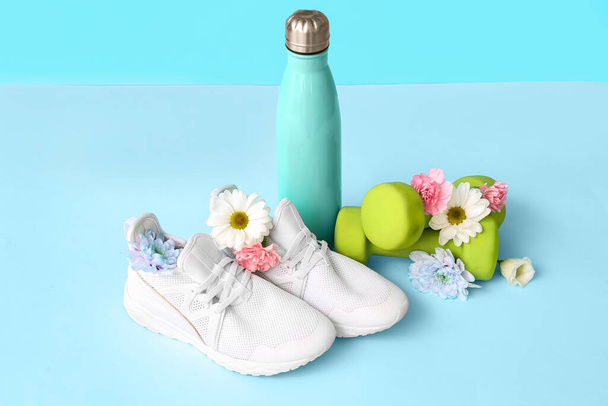 Trampki z wiosennymi kwiatami i butelką na niebieskim tle - Zdjęcie, obraz