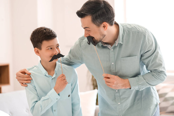 Портрет батька і його маленького сина з паперовими вусами вдома
 - Фото, зображення