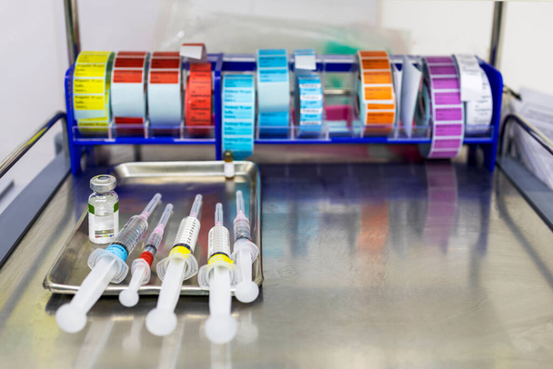 Strzykawka medyczna z kolorową etykietą na tacce ze stali nierdzewnej w szpitalu.Przygotowanie leku do uspokojenia pacjenta przed zabiegiem z rozmytym tłem.. - Zdjęcie, obraz