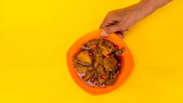 黄色の背景に隔離されたトップビュー,片手で混合野菜のボウルを持ち上げるインドの高齢者の女性,オレンジボウルで野菜グジャラート・ラシヤ・ムティアを混ぜます. - 写真・画像