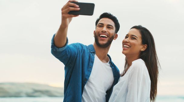 Selfie bebeğine gülümse. Mutlu genç bir çift, gün boyunca sahilde selfie çekerken poz veriyor. - Fotoğraf, Görsel