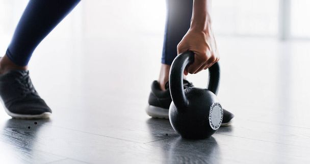 Чем больше поднимаешь, тем сильнее становишься. a woman working out with quettlebells in a gym - Фото, изображение