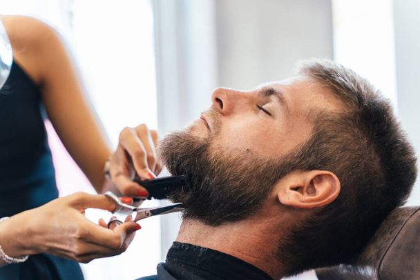 Parrucchiere irriconoscibile che taglia la barba di un uomo in un salone - Foto, immagini