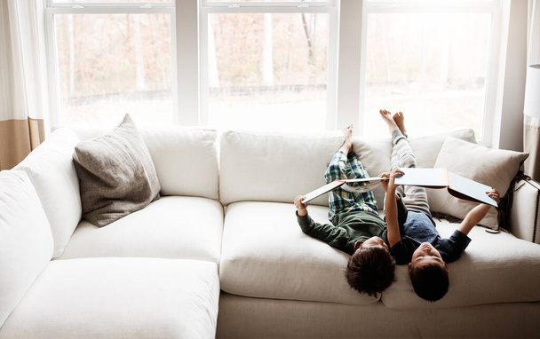 Ideje kihúzni a dugót és elolvasni egy könyvet. két imádnivaló testvér könyvet olvas, miközben együtt pihennek otthon a kanapén. - Fotó, kép