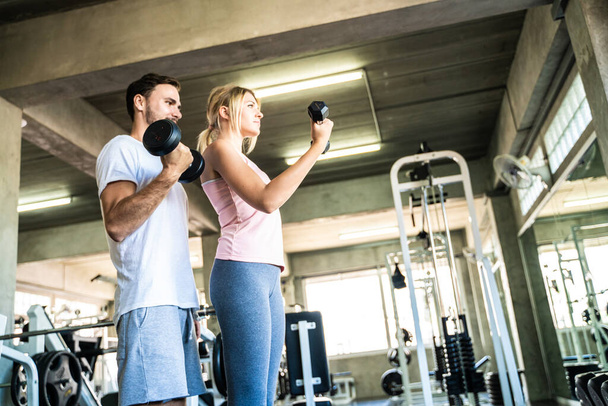 Hombre y mujer haciendo ejercicio con mancuerna en fitnes deporte gimnasio entrenamiento saludable con novio - Foto, imagen