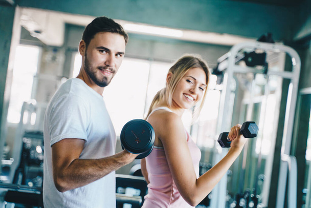 Hombre y mujer haciendo ejercicio con mancuerna en fitnes deporte gimnasio entrenamiento saludable con novio - Foto, Imagen