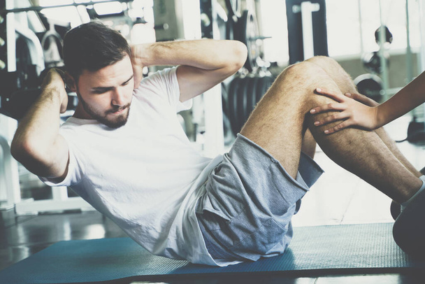 Sport homme assis debout sur tapis de yoga exercice dans la salle de gym aide avec la main de la femme - Photo, image