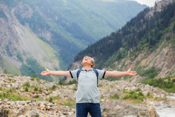 Mutlu orta yaşlı bir adam kollarını açarak dağların arkasına yaslanmış. - Fotoğraf, Görsel