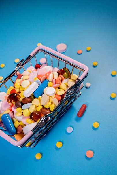 Various capsules, pills and medicines in a shopping cart on a blue background. Health care, treatment. The concept of buying pills and buying medicine. - Foto, Imagem