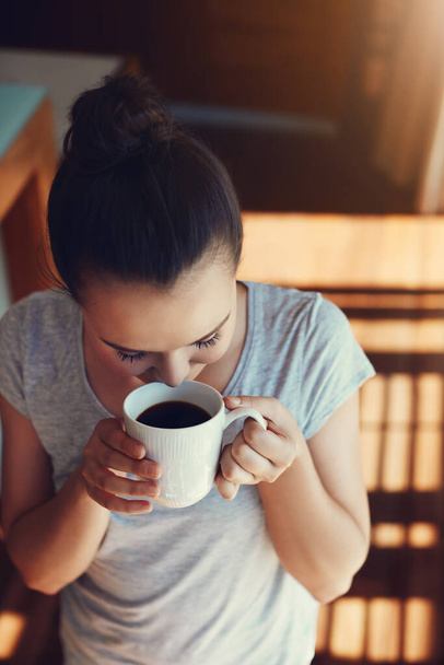 Enjoying that first sip. an attractive young woman enjoying her morning coffee while standing in the kitchen at home - Foto, Bild