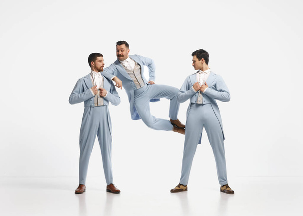 Gentlemen. Portrait with three men wearing elegant clothes jumping and dancing over white background. Concept of historical remake, comparison of eras, retro, vintage, emotions, mood, ad - 写真・画像