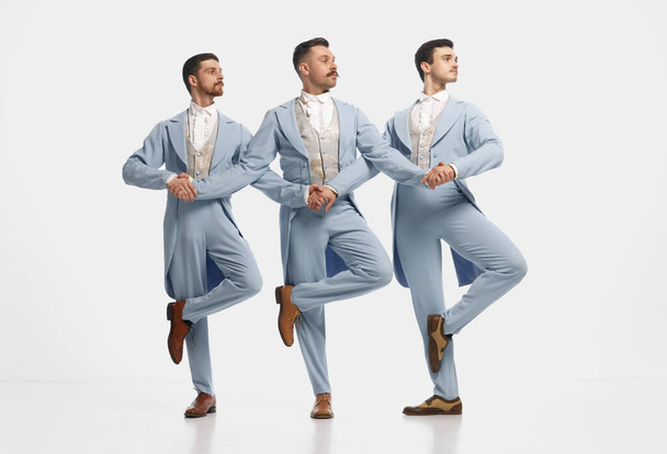 Mužský balet. Portrét se třemi muži v elegantním oblečení stojící v řadě a tančící na bílém pozadí. Koncept historické remake, srovnání éry, retro, vintage, emoce, show - Fotografie, Obrázek