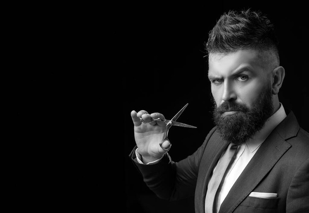 Confident barber at barbershop. Barber and hairdresser salon. Beard care, perfect beard. Bearded man in formal business suit. Brutal male hipster cut hair with hairdressing scissors - copy space. - Photo, Image