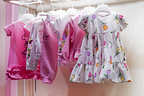 Niedliche Sommerkleider für Kinder mit floralen Prints auf einem Kleiderbügel, waagerecht - Foto, Bild