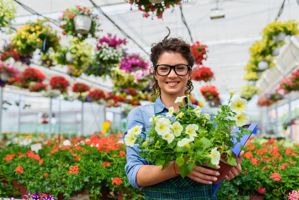 young beautiful woman working with flowers in greenhouse - Foto, imagen