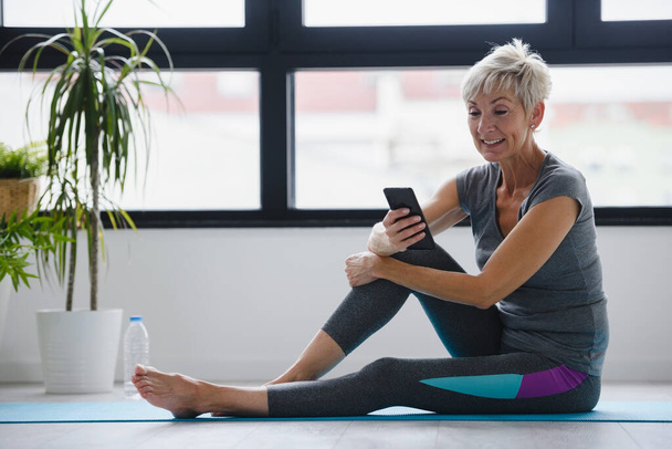 старша жінка сидить на йога килимок з телефоном
  - Фото, зображення