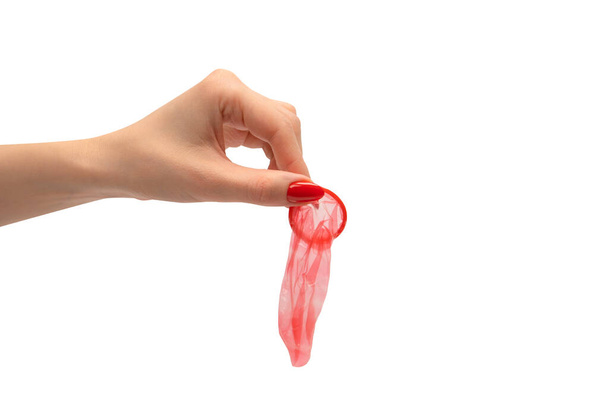 A red condom in a woman hand with red nails isolated on a white background.  - Fotó, kép