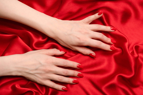 Une main de femme avec des ongles rouges essaie d'arracher le tissu de soie rouge.  - Photo, image