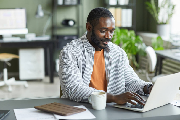 Porträt eines erwachsenen schwarzen Mannes, der zu Hause im Büro arbeitet und Laptop und Kopierraum benutzt - Foto, Bild