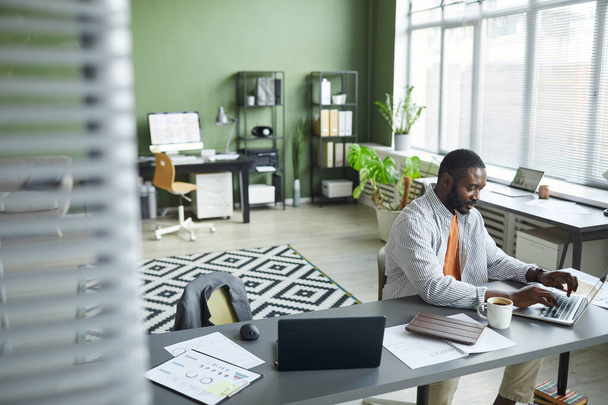 Korkea kulma muotokuva aikuisten musta mies työskentelee kotitoimistossa moderni sisustus ja kannettavan tietokoneen, kopioi tilaa - Valokuva, kuva