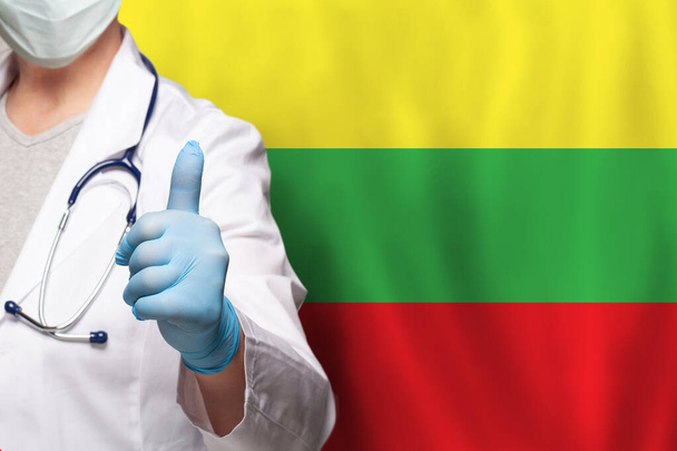 Lithuanian doctor's hand showing thumb up positive gesture on flag of Lithuania background - 写真・画像