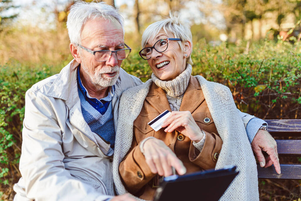 senior couple sitting on bench in the park, making online order - Photo, Image