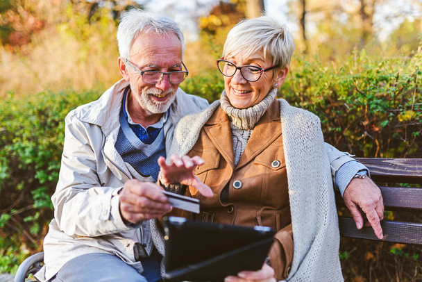 coppia anziana seduta sulla panchina nel parco, facendo ordine online - Foto, immagini