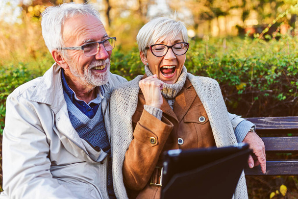 feliz pareja de ancianos sentado en el banco en el parque haciendo selfie - Foto, Imagen