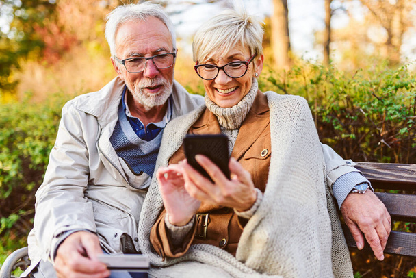 couple âgé assis sur le banc dans le parc, faire une commande en ligne - Photo, image