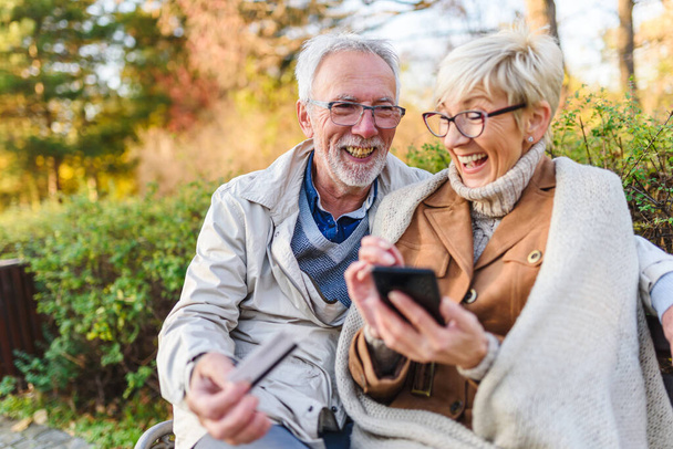 старша пара сидить на лавці в парку, роблячи онлайн замовлення
 - Фото, зображення