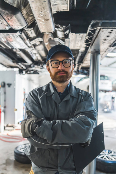Caucasian mechanic with glasses holding notes from cars inspection and looking at the camera, medium vertical shot. High quality photo - Foto, imagen