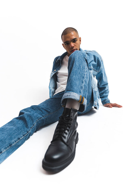 African male model sitting on the floor in white studio wearing full denim outfit . High quality photo - Foto, Imagem