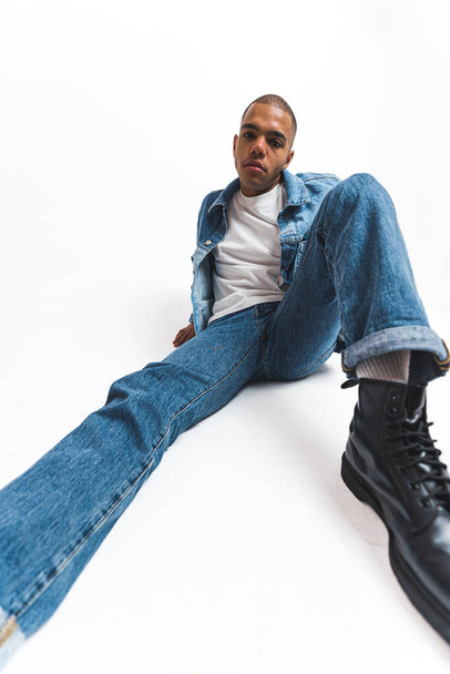 African male model sitting on the floor in white studio with his legs close to the camera. High quality photo - Photo, Image