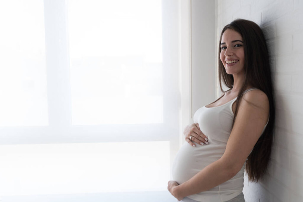 giovane bella donna incinta posa vicino alla finestra - Foto, immagini