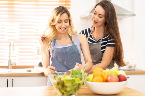 happy and smile lesbian couple cooking salad in the kitchen. salad in glass bowl with sweet smile while cooking together. pride month to promote equality and differences of homosexual. - Фото, изображение